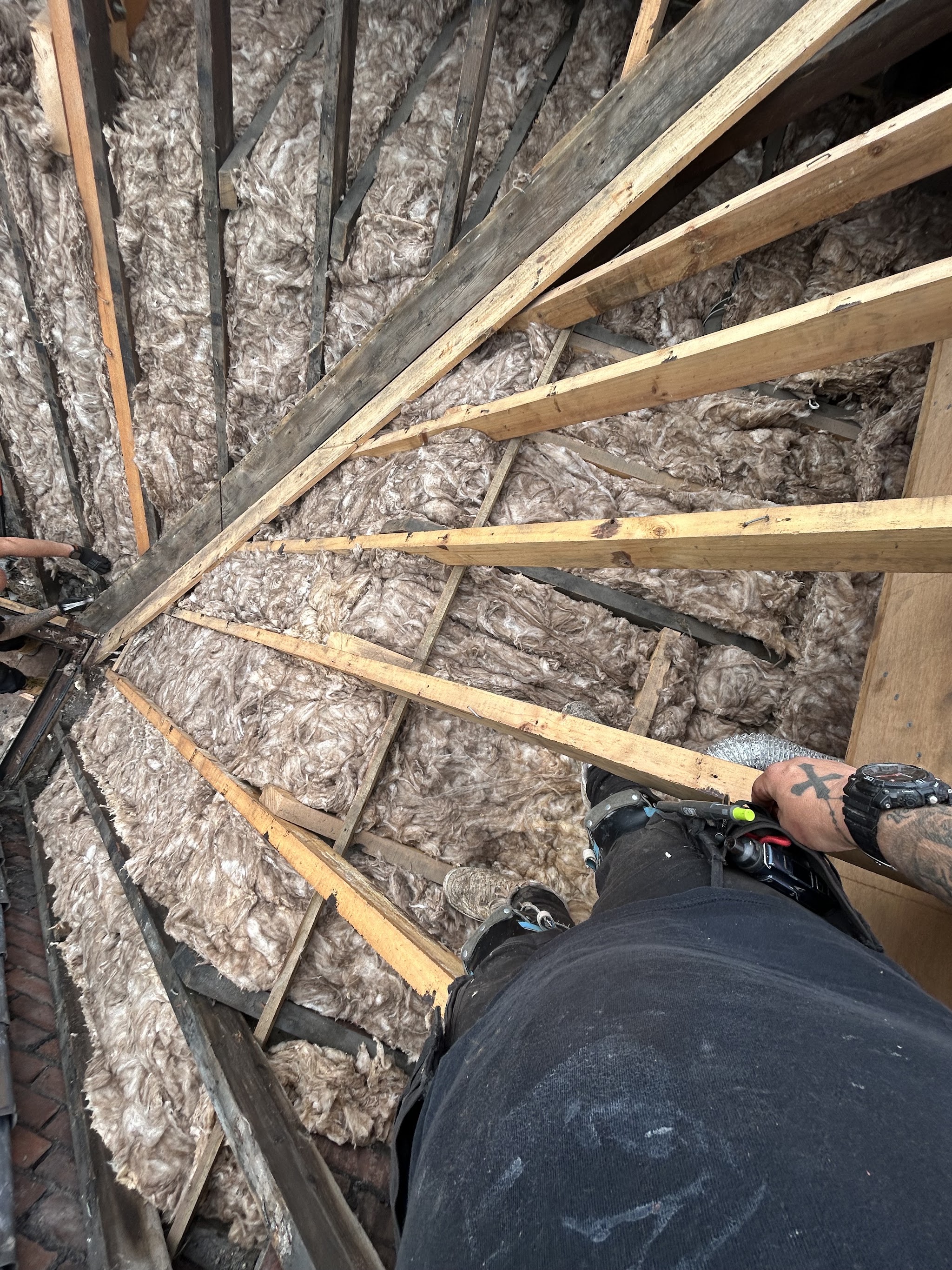 Loft insulation fitted between the rafters, a roofer's legs in the foreground