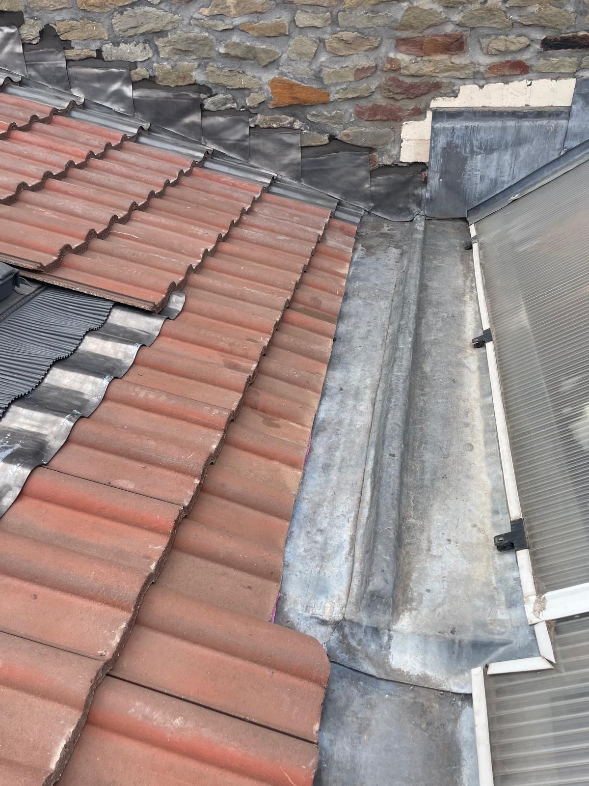 Red interlocking roof tiles meeting a lead-lined valley beside a stone wall