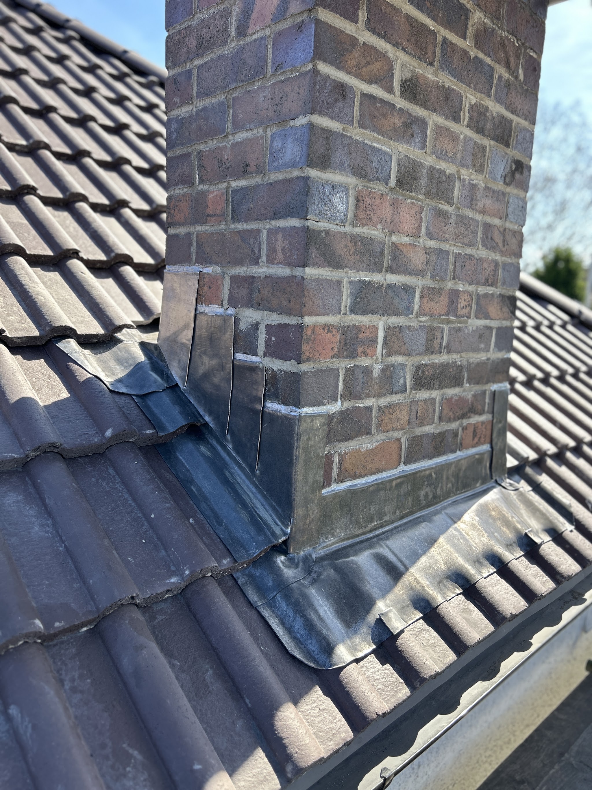 Lead flashing and soakers dressed round a brick chimney on a grey tiled roof