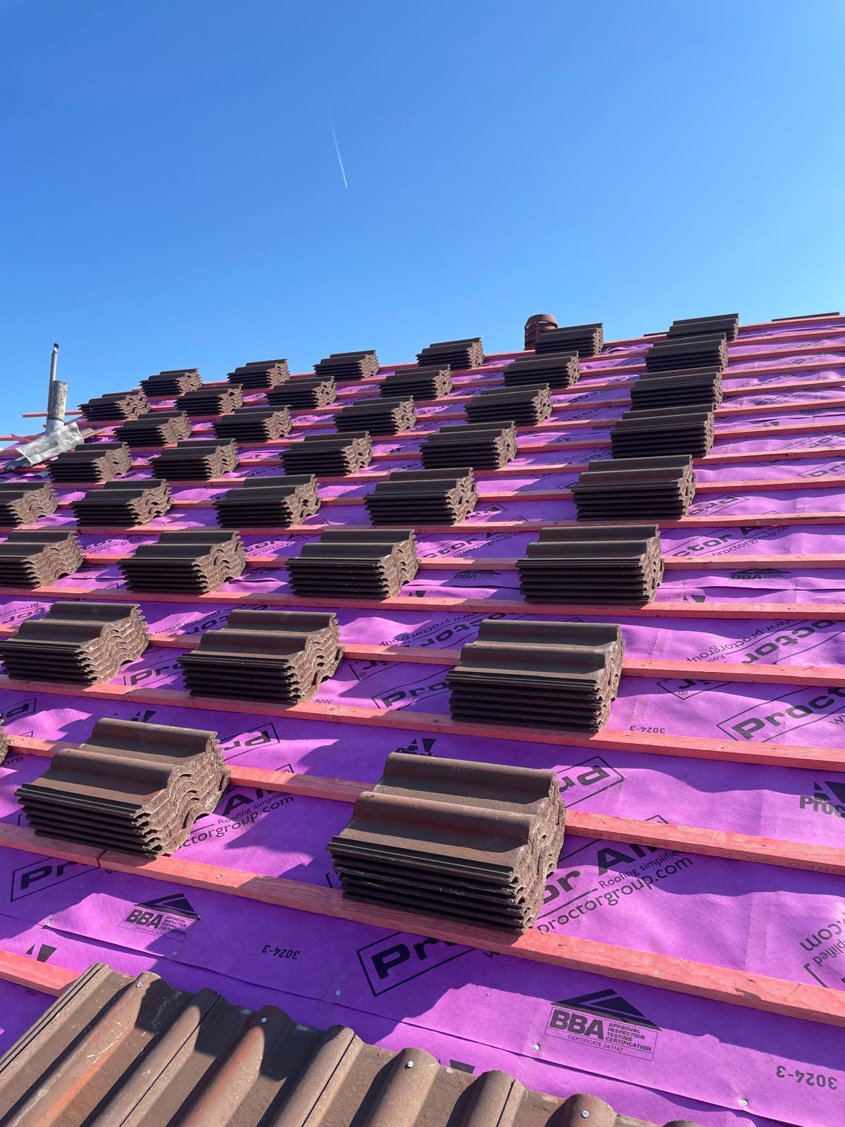 Stacks of new tiles loaded out on battens over a purple breathable membrane