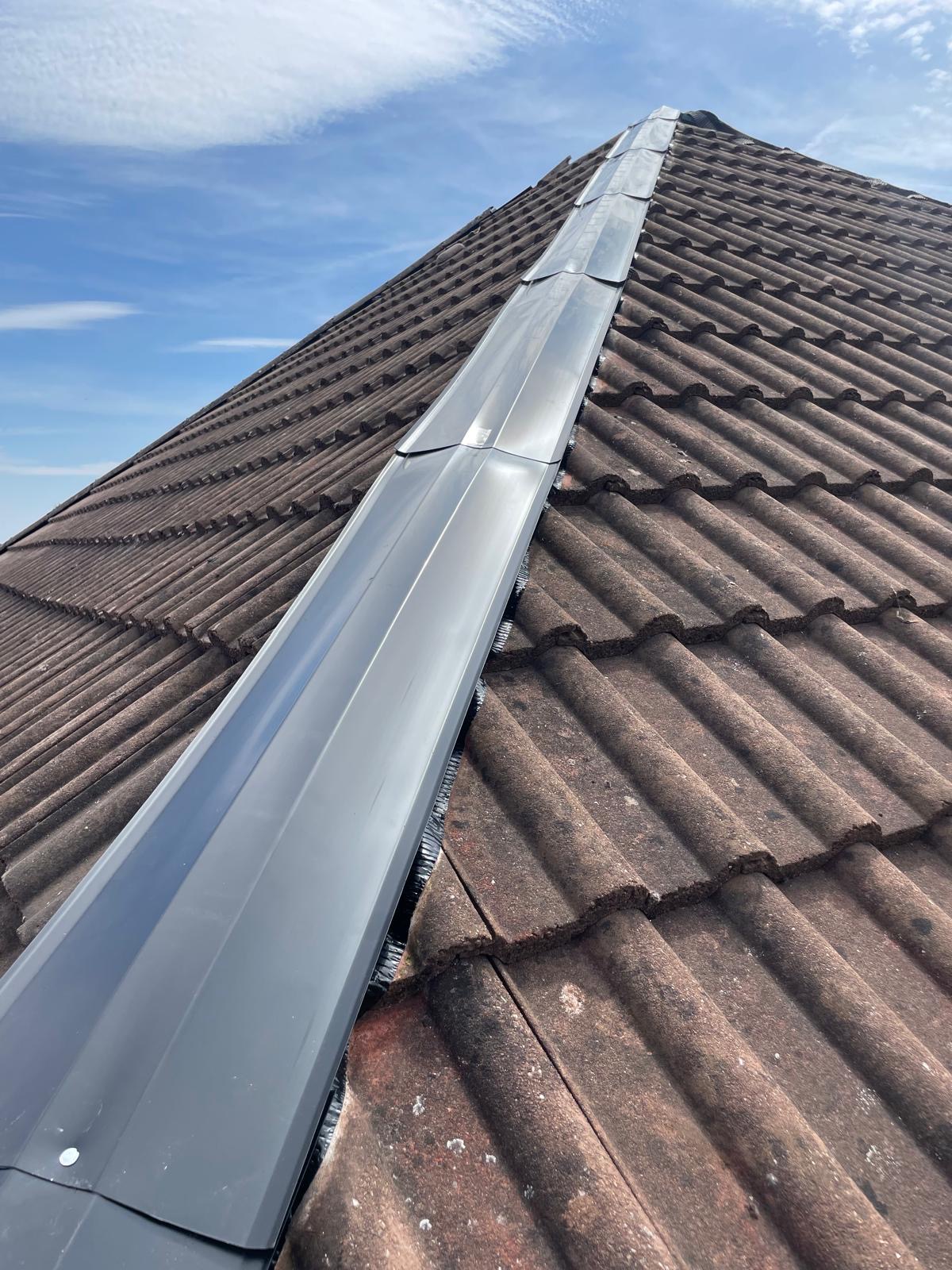 A dry-fixed ridge running up a brown tiled roof against a blue sky