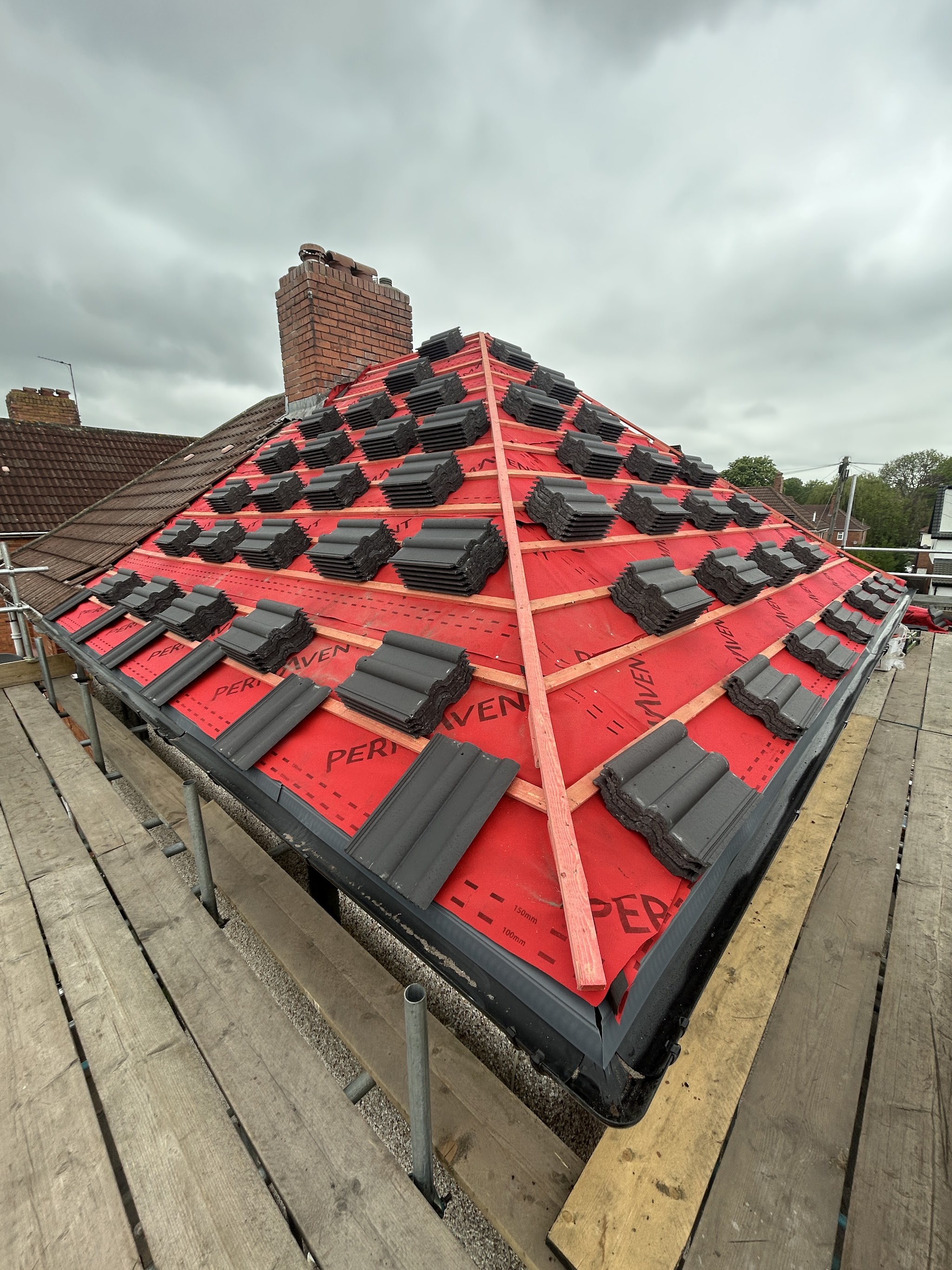 A hipped roof in red membrane with tiles loaded out, scaffold boards in front