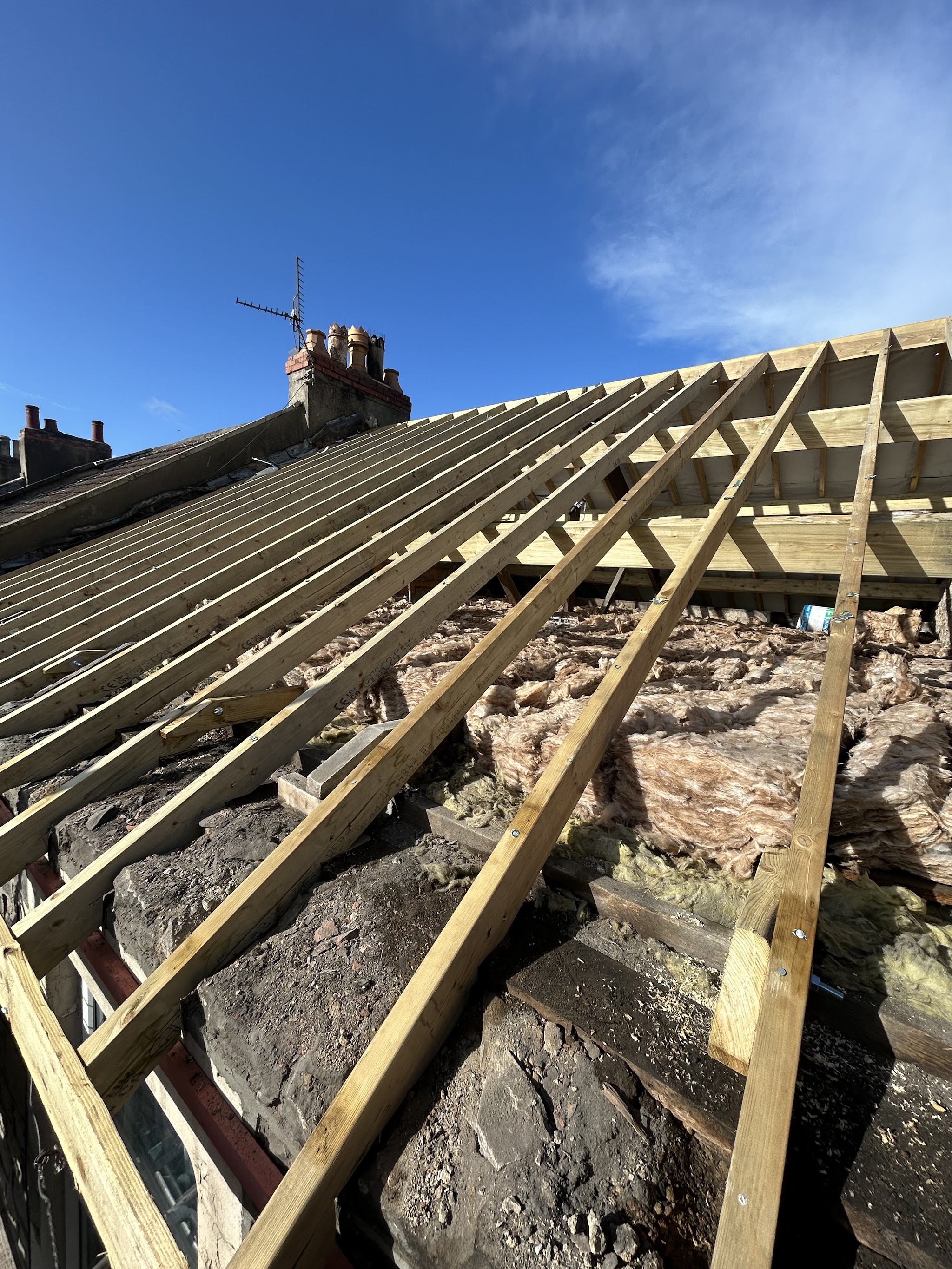 An old roof stripped back to new timber battens, with the chimney stack behind